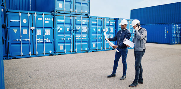 Workers discussing plans in front of blue cargo containers